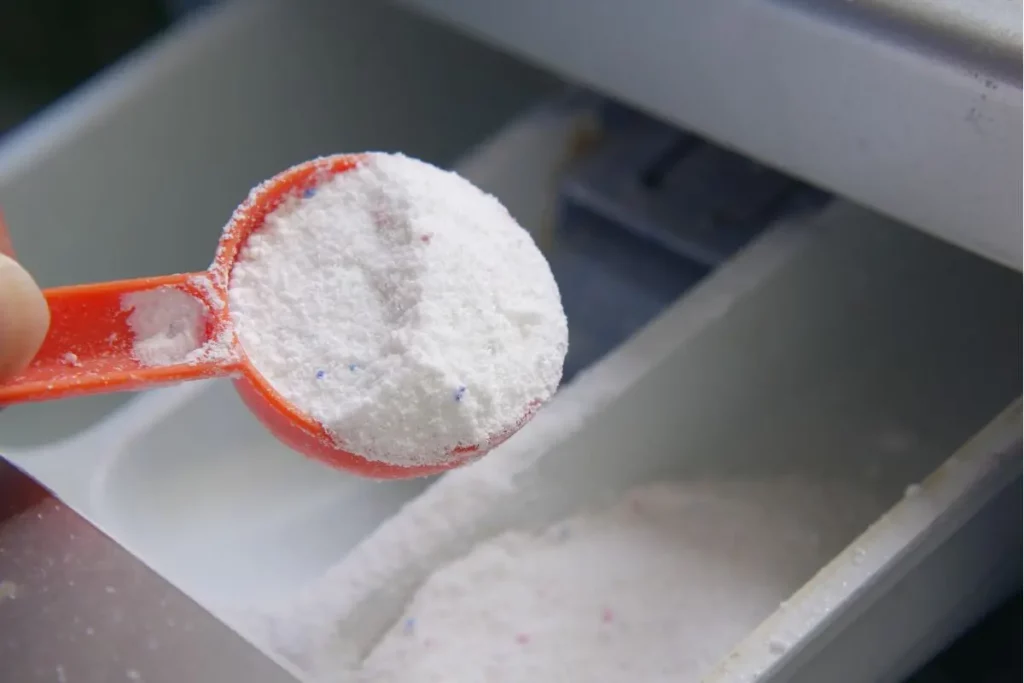 Cuillère de bicarbonate de soude versée dans une machine à laver.