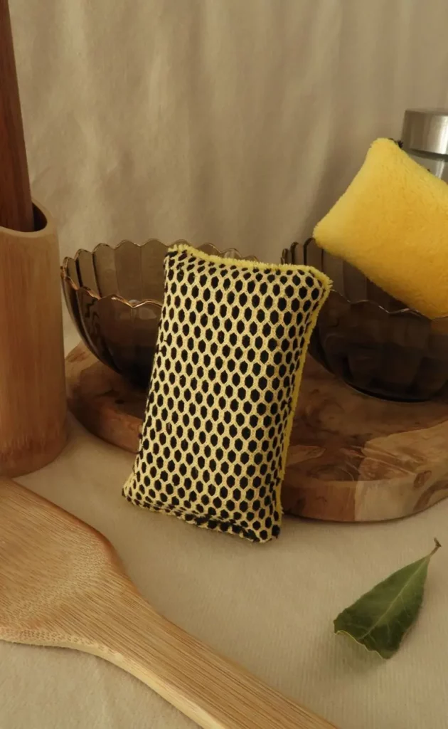 Éponge lavable jaune posée sur un plan de cuisine avec des ustensiles.
